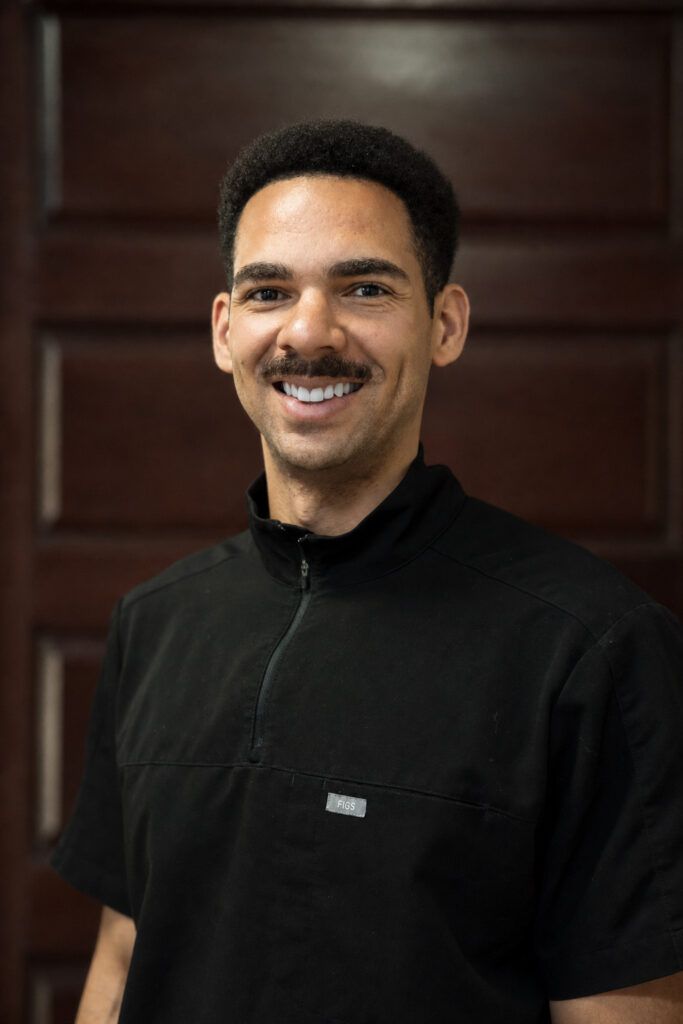 Dr. Josh Thomas smiling in black jacket against wood paneled office background