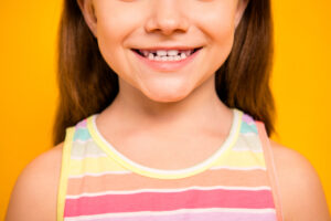 Cropped photo of charming, kid having toothy smile wearing tank-top isolated over yellow background